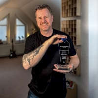 Vorschaubild: Auf diesem Bild ist Friedrich Kalpenstein in seiner Schreibwerkstatt zu sehen. In seinen Händen hält er die Auszeichnung seines Verlags für eine Million verkaufte Bücher