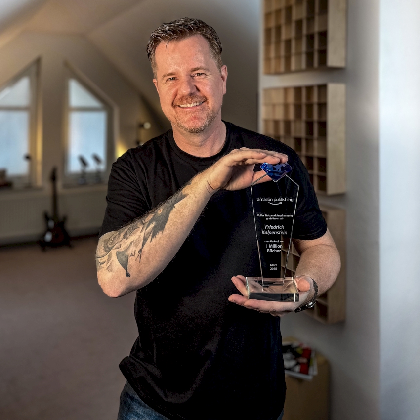 Auf diesem Bild ist Friedrich Kalpenstein in seiner Schreibwerkstatt zu sehen. In seinen Händen hält er die Auszeichnung seines Verlags für eine Million verkaufte Bücher